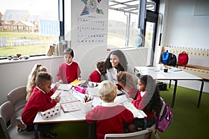 A group of infant school kids sitting at a table in a classroom with their female teacher