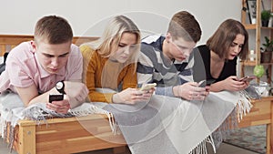 Group of internet-addicted teenegers lying on bed and looking at smartphones