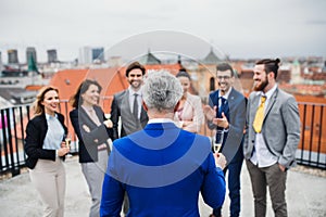 A group of joyful businesspeople having a party outdoors on roof terrace in city.