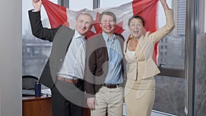 Group of joyful happy business people posing with Canadian flag in office. Cheerful men and woman holding national