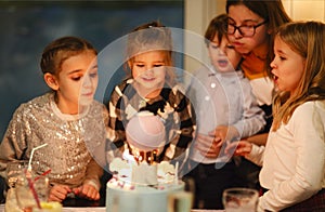 Group of joyful little kids celebrating birthday party and blowing candles on cake