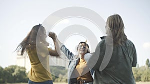 Group of joyful relaxed hippies friends spinning and jumping on sunny summer day outdoors. Three carefree Caucasian