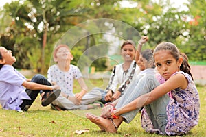 Group of kids bulling girl at park during summer camp - Little girl looking camera, sitting lonely while friends playingand having photo