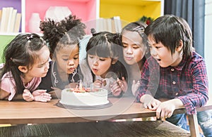 Group of kids enjoying a birthday party blowing out the candle on cake.