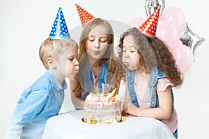 Group of kids in festive cap blowing the candle,making a wish. Celebration. Birthday party