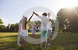 Group of a kids friends playing outside in the park standing in a circle and holding hands up.