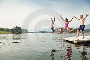 Group of kids jumping off the dock into the lake together during a fun summer vacation.
