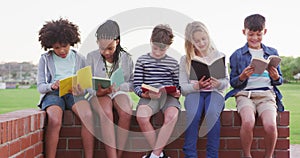 Group of kids reading books while sitting on a brick wall