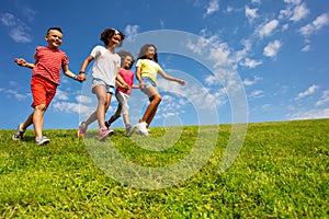 Group of kids run on the grass field holding hands