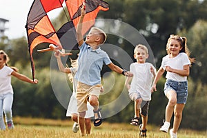 Group of kids are running and playing with kite on green field