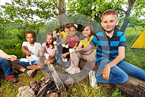 Group of kids sit near bonfire with marshmallow