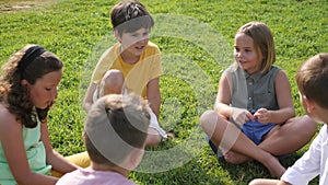 Group of kids sitting on field's green grass in summertime.