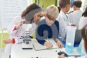 Group of kids students using microscope writing on notebook at laboratory classroom