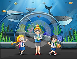 Group of kids watching fishes at aquarium excursion with woman teacher