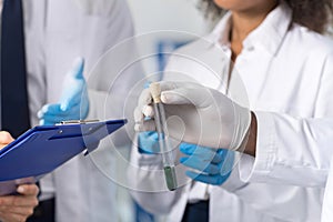 Group Of Laboratory Scientists Examining Test Tube Making Notes Discuss Experiment Or Reseach Results Wearing Protective