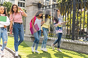 Group of Latina teen friends students walking with their backpacks, notebooks, laptop and cell phone on their way to high school.