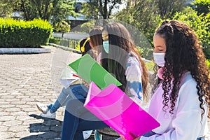 Group of Latina teenagers with a mask studying outdoors and social distancing for coronavirus prevention