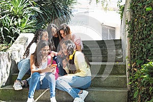 Group of Latina teenage girls students interacting with their cell phones sitting in some bleachers outdoors photo