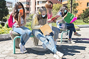 Group of latinx teenagers studying in notebooks and cell phone with mask on campus photo