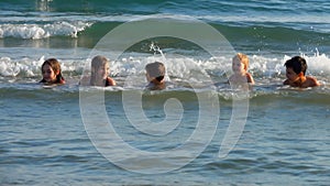 Group of laughing children are laying on their stomacks in sea waves on a beach
