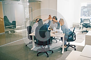 Group of laughing coworkers high fiving during an office meeting