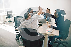 Group of laughing coworkers high fiving during an office meeting