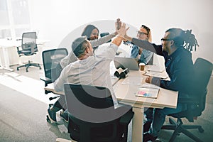 Group of laughing coworkers high fiving during an office meeting photo