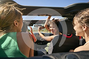 Group Of Laughing Female Friends Having Fun In Open Top Car On Road Trip
