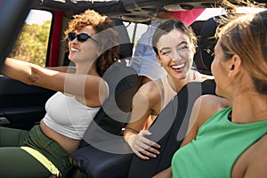 Group Of Laughing Female Friends Having Fun In Open Top Car On Road Trip