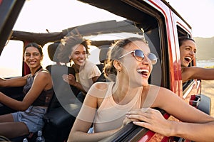 Group Of Laughing Female Friends Having Fun In Open Top Car On Road Trip