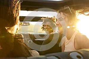 Group Of Laughing Female Friends Having Fun In Open Top Car On Road Trip