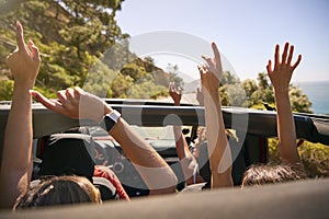 Group Of Laughing Female Friends Putting Hands Through Sunroof Open Top Car On Road Trip