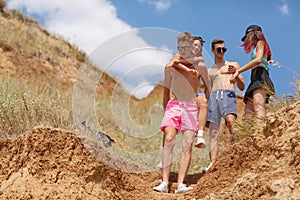 A group of laughing friends stands on a field, beautiful girls and boys on a vacation on a natural blurred background.