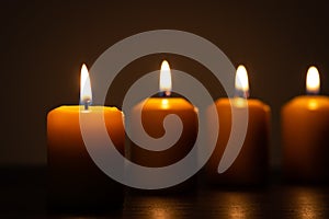 Group of lit candles in a row burning in the darkness