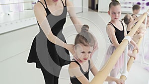 Group of little ballet dancers in pink leotards and tutu skirts hanging on ballet barre and doing exercise in dance