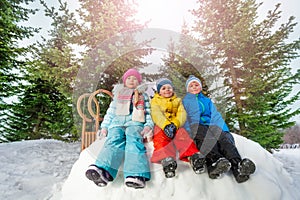 Group of little children sit on snow wall in park