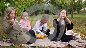 A group of little girls on a picnic in the park in summer or autumn blow soap bubbles