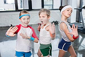 Group of little kids in sportswear exercising and posing at camera in gym