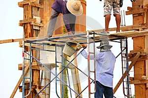 group of local worker stood on scaffolding without protective gear pouring cement into the wooden formwork