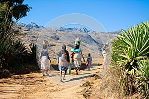 A group of Malagasy people carrying loads on their heads walking on a road.