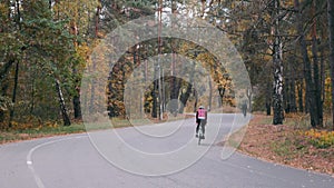 Group of male and female cyclists in cycling apparel riding on road bicycle in empty autumn park. Young sportive women and men har
