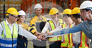 Group of male and female factory labor join hands together after finish meeting. Everyone wearing safety uniform and helmet.