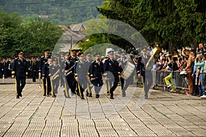 Group of male musicians in military uniforms playing large instruments, marching in a parade