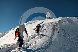 Group of male skiers with backpacks and ski equipment walking up on snowy ridge