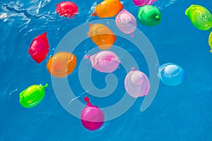 Group of many colorful plastic water balloons floating in the water of a pool to entertain their children on summer vacations