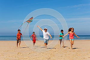 Group of many kids run with kite on a sand beach