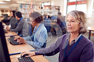 Group Of Mature Adult Students In Class Working At Computers In College Library