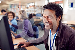 Group Of Mature Adult Students In Class Working At Computers In College Library