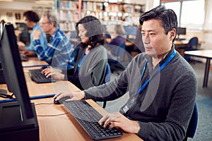 Group Of Mature Adult Students In Class Working At Computers In College Library