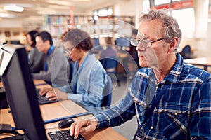 Group Of Mature Adult Students In Class Working At Computers In College Library